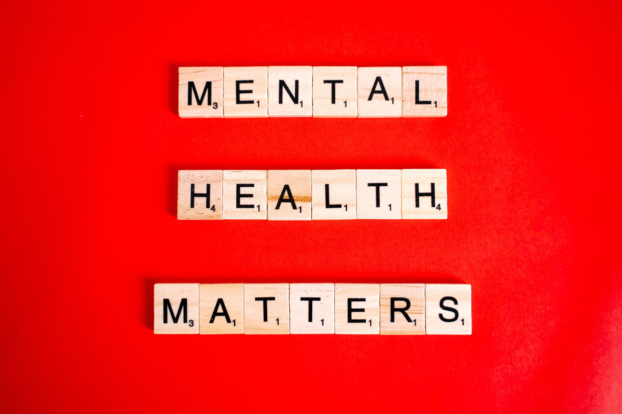 “Mental Health Matters” is spelled out using tiles from a Scrabble board. Behind it is a red background.