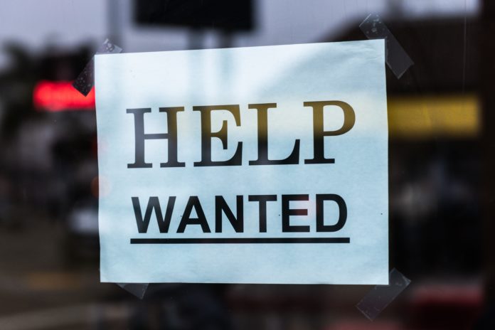 A help wanted sign is posted with black lettering on white paper.