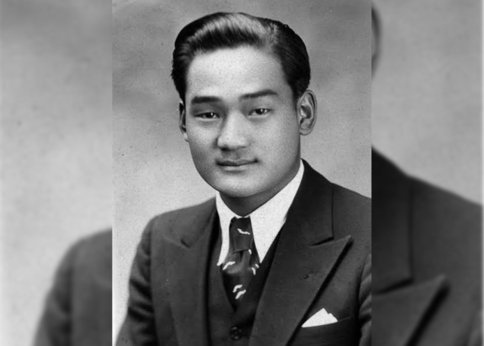 A young man poses for a picture wearing a suit and tie in a black and white photo.