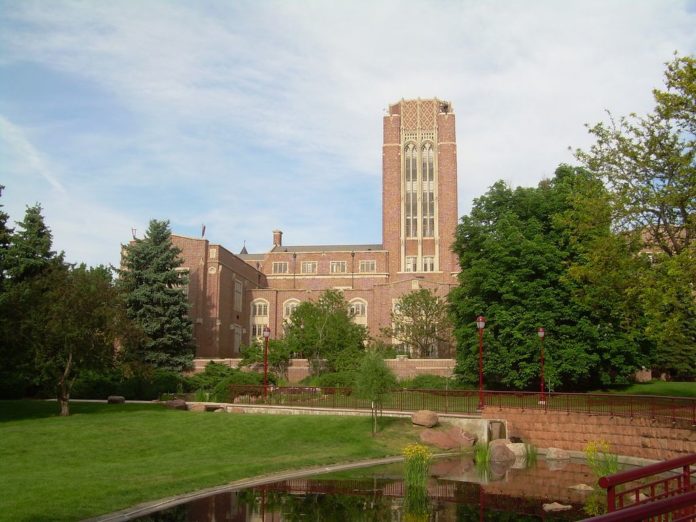 A brick building can be seen in the background with a large tower looming above it. A pond can be seen in the foreground.