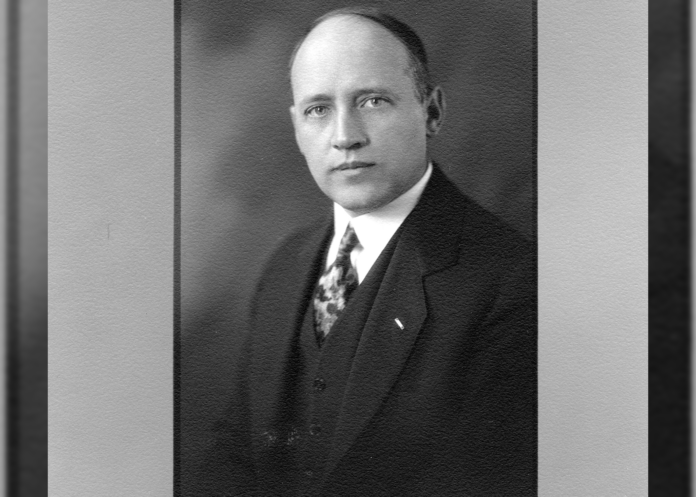 Philip Van Cise sits for an official portrait. He is wearing what looks like a three-piece suit and tie with a white collared shirt and a small rectangular collar pin.