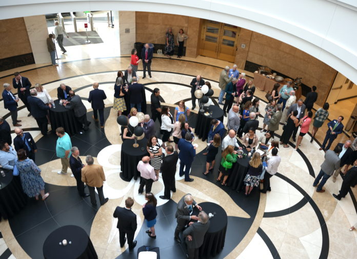 An aerial photograph of people wearing formal clothes gathered in a large rotunda with ornate stone floors in the shape of a columbine. There are small tables with black tablecloths and white and black balloons.