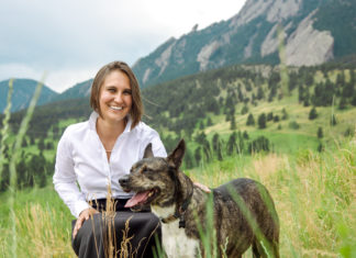 The Animal Law Firm Continues Expanding A woman kneels as she poses with a dog. Trees and part of a mountain can be seen in the background.