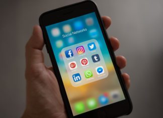 Aspen School District Sues Social Media Companies Claiming Harm to Students A hand holds an iPhone open to a folder titled ‘social networks.’ The folder has app icons for Facebook, Instagram, Twitter, Google, Pinterest, Tumblr, LinkedIn, Whatsapp and Facebook Messenger.