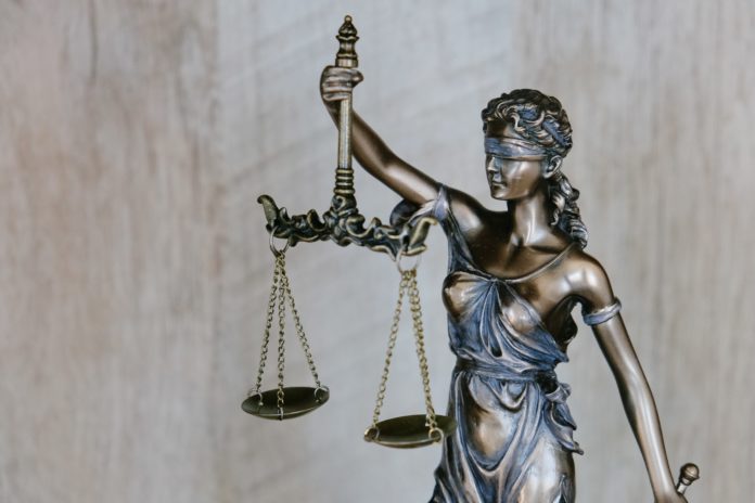 tingey-injury-law-firm-DZpc4UY8ZtY-unsplash A bronzed statue of lady justice holds her scales aloft while a sword dangles loosely from her other hand.
