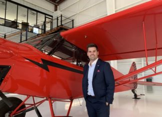 Aviation Law Takes Off A man wearing a suit coat stands next to a small red plane.