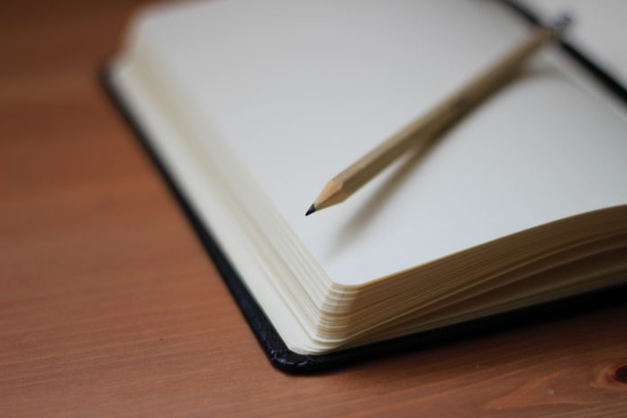 A pencil rests on top of a blank notebook page.