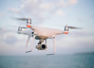The Ins and Outs of Drone Law A small white machine with propellers attached to it flies in the air. What appears to be a camera is attached.