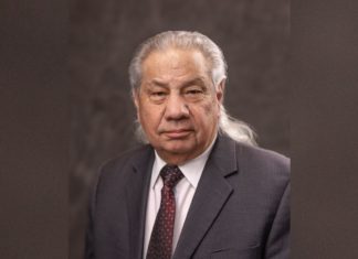 Boulder Attorney John Echohawk Recognized for Career of Civil Rights Work An older man with long gray hair behind his shoulders in a gray suit and red tie looks at the camera with a serious expression.