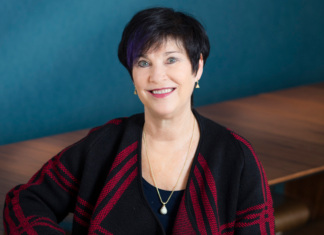 Attorney, Former Judge Robbie Barr Set to Retire After Prolific Career A woman sits in front of a desk. She has brown hair and is wearing earrings and a necklace and has a black and red coat on.