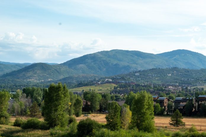 Steamboat Springs is nestled at the base of large hills with green trees in the foreground giving small glimpses at buildings that look like condos.