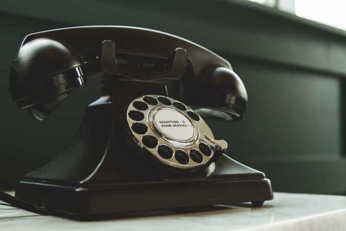 Black rotary telephone on white surface.