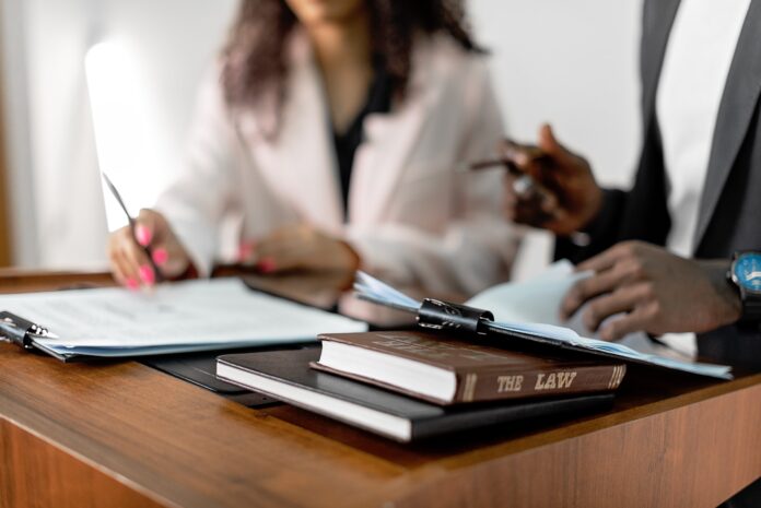 Two people sit at a desk with papers and a law book.