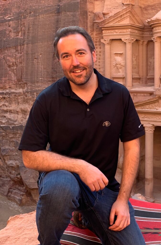 2024 Lawyer of the Year Winner Jason Slothouber taking a knee in a University of Colorado Boulder polo in front of the Petra historical site. 