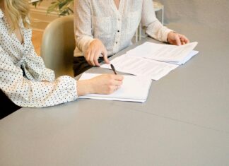 ABA Ethics Committee Releases Opinion Addressing Conflicts of Interest Under Model Rule 1.18 two people are reviewing and signing papers on a conference table while speaking to each other