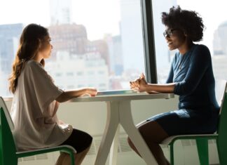 Law Firms Work to Close the Gender Gap in Leadership and Management Two professional women sit at a table having a conversation.