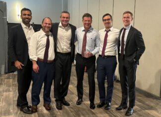 Giovanni Sanchez of Bartlit Beck Recounts the Trial Leading to an $847 Million Patent Infringement Verdict Against Verizon Giovanni Sanchez, Nosson Knobloch, Glen Summers, John Hughes, Taylor Kelson and Luke Beasley smile for a photo in various states of formal wear in an unadorned meeting room.