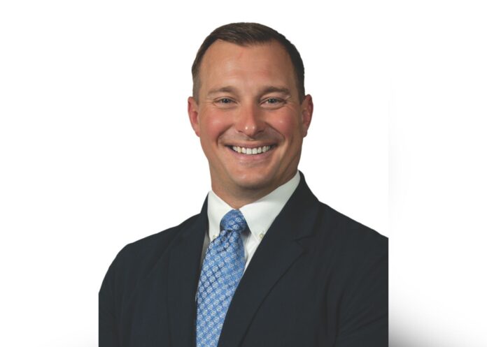 Ben Busboom Editorial Benjamin Busboom smiles at the camera in a headshot photo, wearing a blue patterned tie and a navy suit jacket.