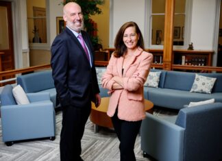Lathrop GPM and Hopkins Carley Managing Partners Discuss Their Firms’ Combination Cameron Garrison and Jennifer Johnson stand next to each other in the welcome area of an office. Garrison wears a navy suit and Johnson wears a tan jacket. In the background are couches and short bookshelves.