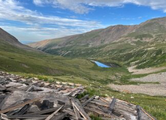 New Federal Bill Aims to Eliminate Liability for Abandoned Mine Cleanups A green valley in the mountains with a lake in the center, with debris from an inactive mine in the foreground.