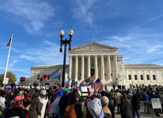 U.S. Supreme Court Hears Arguments on Tennessee’s Gender-Affirming Care for Minors Ban Hundreds of people gather in front of the U.S. Supreme Court. Multiple flags representing the LGBTQ+ and transgender communities, as well as an American flag, are held by protestors.