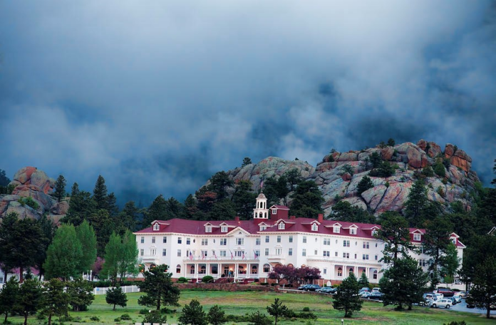Stanley - Taft The Stanley Hotel, a large white building with a red roof, sits in front of a hillside with dark clouds roiling above.